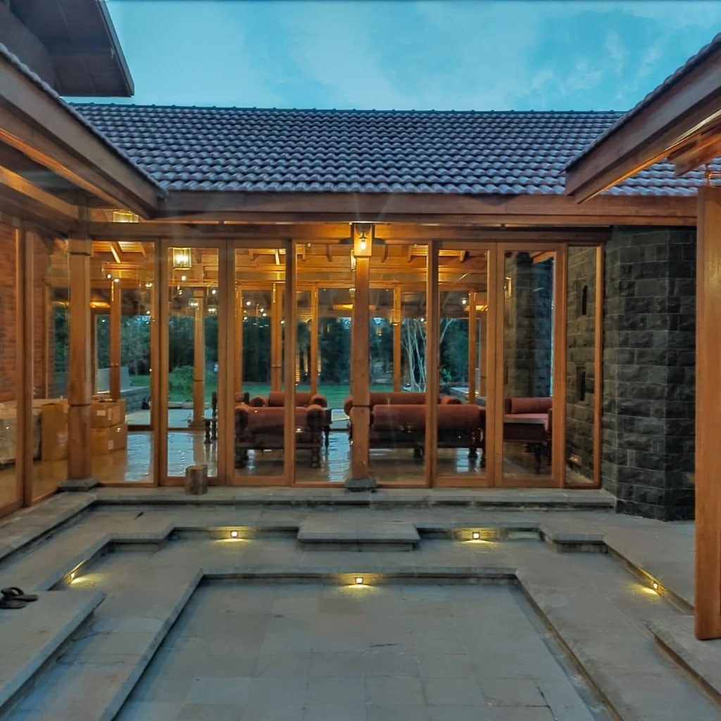 Sunken stone courtyard with timber-and-glass lounge at dusk